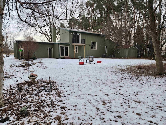 snow covered back of property with a shed and a balcony