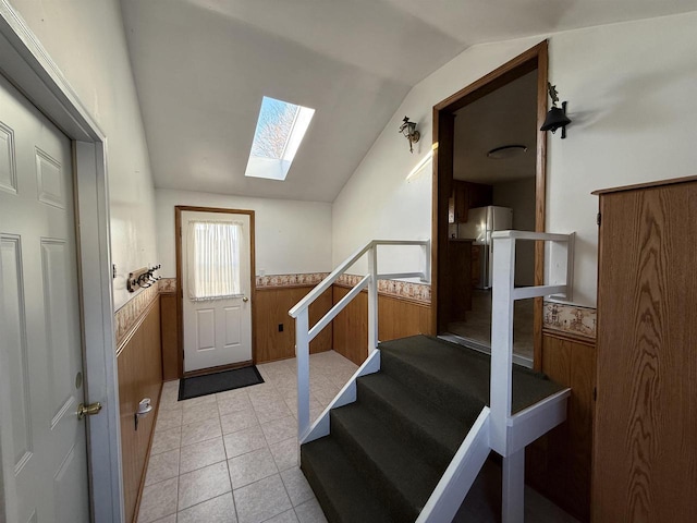 stairs featuring vaulted ceiling with skylight, tile patterned flooring, and wood walls