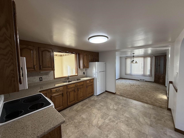 kitchen with decorative light fixtures, white fridge, tasteful backsplash, sink, and light colored carpet