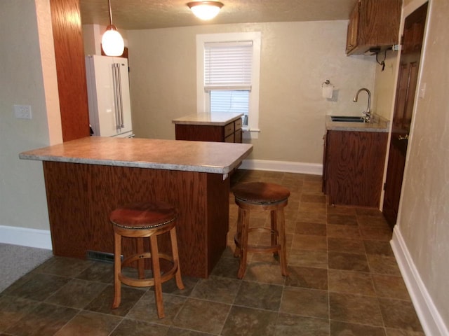 kitchen featuring pendant lighting, a kitchen bar, kitchen peninsula, and sink