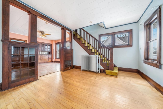 unfurnished living room with decorative columns, a wealth of natural light, radiator, and light wood-type flooring