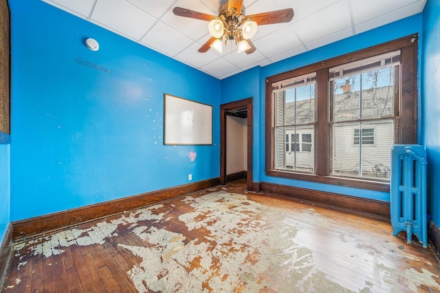 spare room featuring radiator, ceiling fan, hardwood / wood-style floors, and a drop ceiling