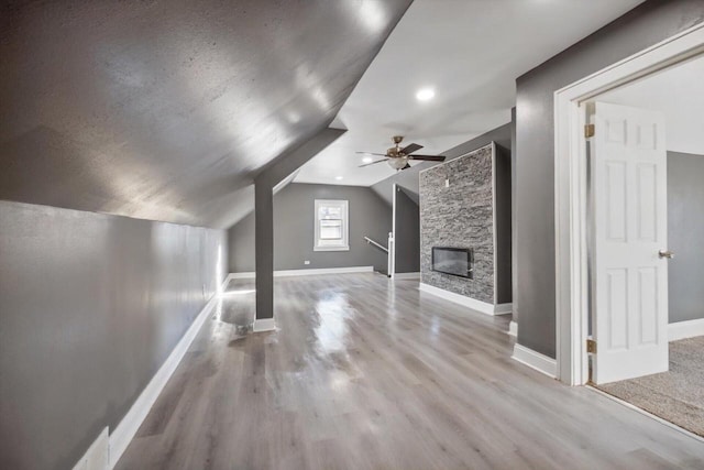 bonus room featuring a textured ceiling, a stone fireplace, vaulted ceiling, ceiling fan, and light hardwood / wood-style flooring