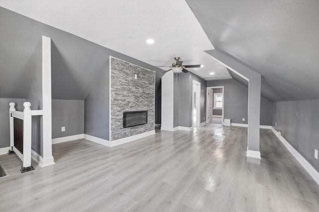 unfurnished living room featuring vaulted ceiling, ceiling fan, light hardwood / wood-style flooring, and a stone fireplace