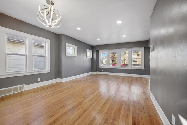 empty room with a notable chandelier and light hardwood / wood-style floors