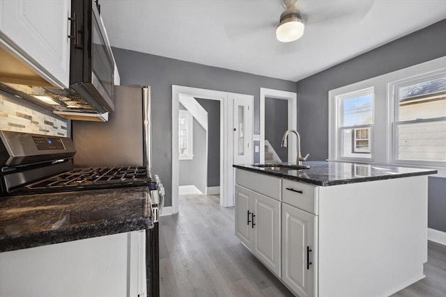 kitchen with white cabinetry, tasteful backsplash, sink, stainless steel range with gas cooktop, and a center island with sink