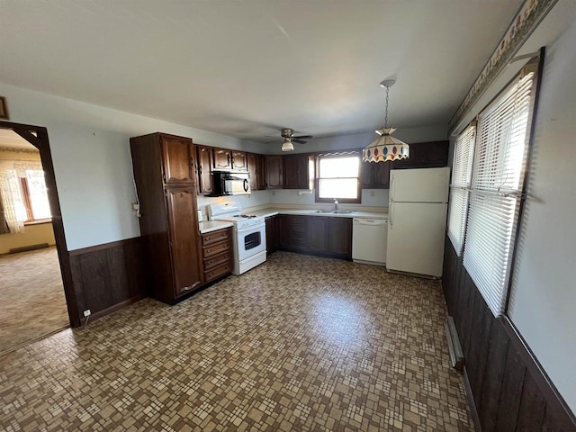 kitchen with ceiling fan, pendant lighting, sink, wooden walls, and white appliances