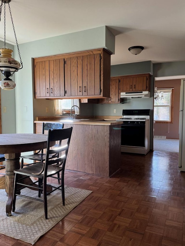 kitchen featuring gas range, dark parquet floors, hanging light fixtures, white refrigerator, and sink