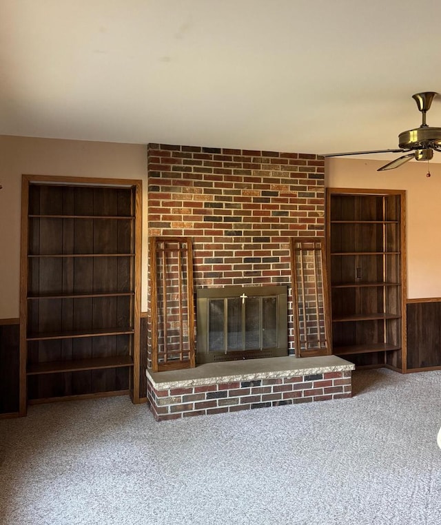 unfurnished living room with carpet, ceiling fan, a fireplace, and wooden walls