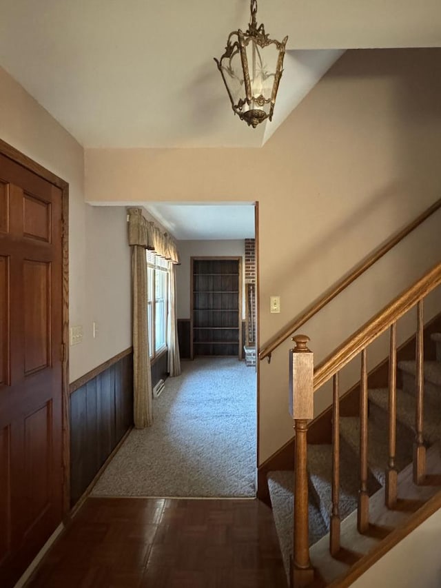 entrance foyer with dark parquet flooring, wooden walls, and an inviting chandelier