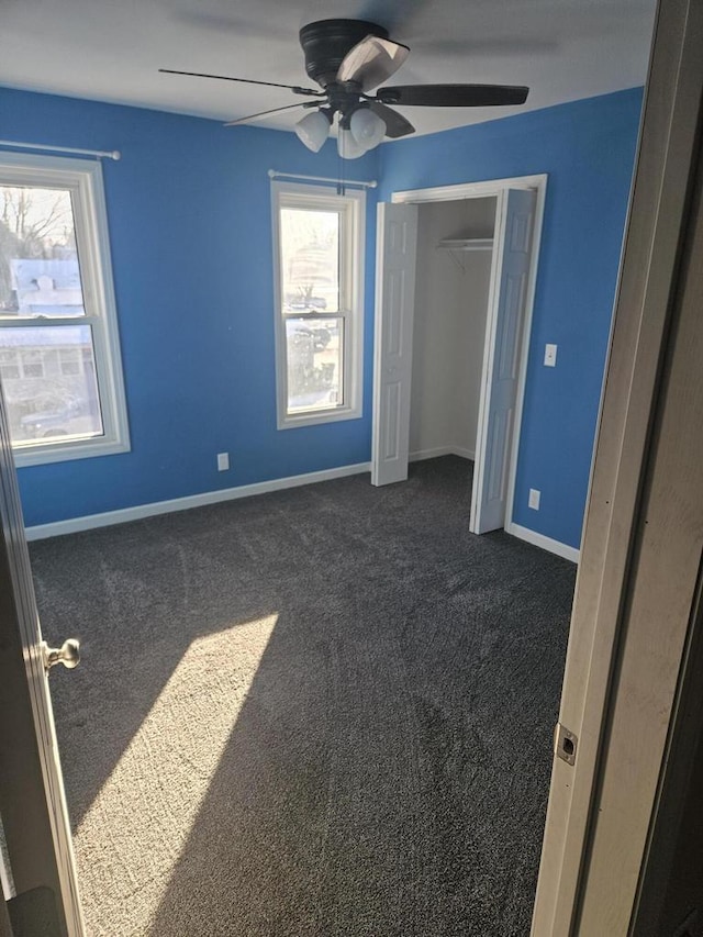 unfurnished bedroom with ceiling fan, a closet, dark colored carpet, and multiple windows