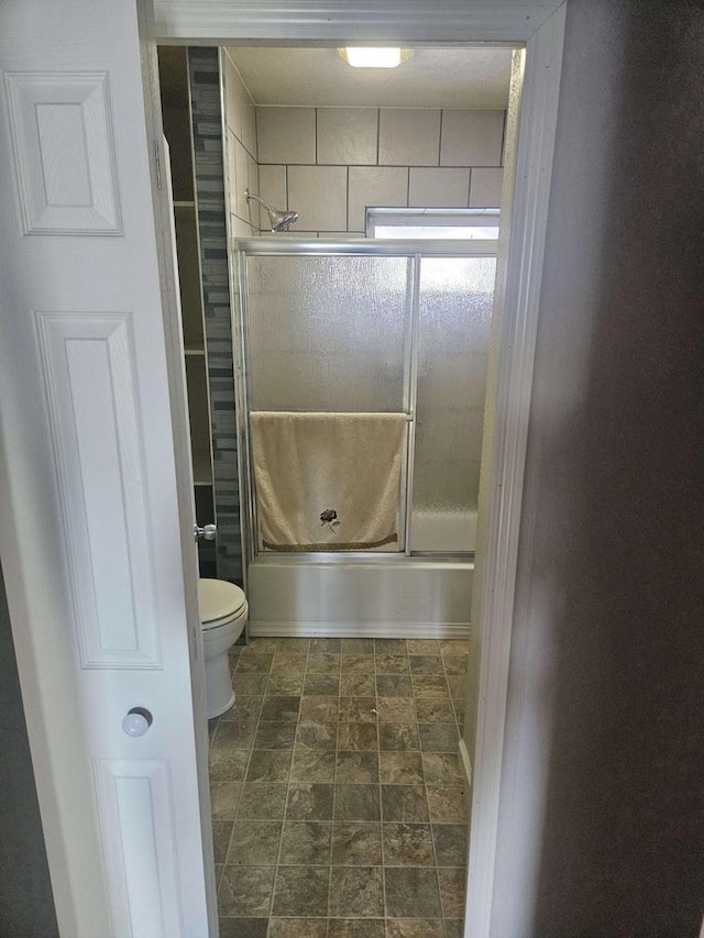 bathroom featuring toilet and shower / bath combination with glass door