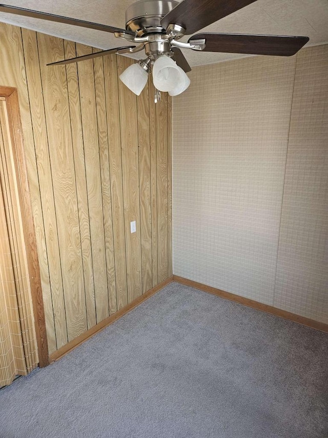 carpeted spare room featuring ceiling fan and wood walls