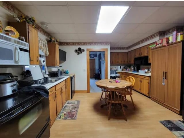 kitchen featuring black appliances, a drop ceiling, and light hardwood / wood-style floors