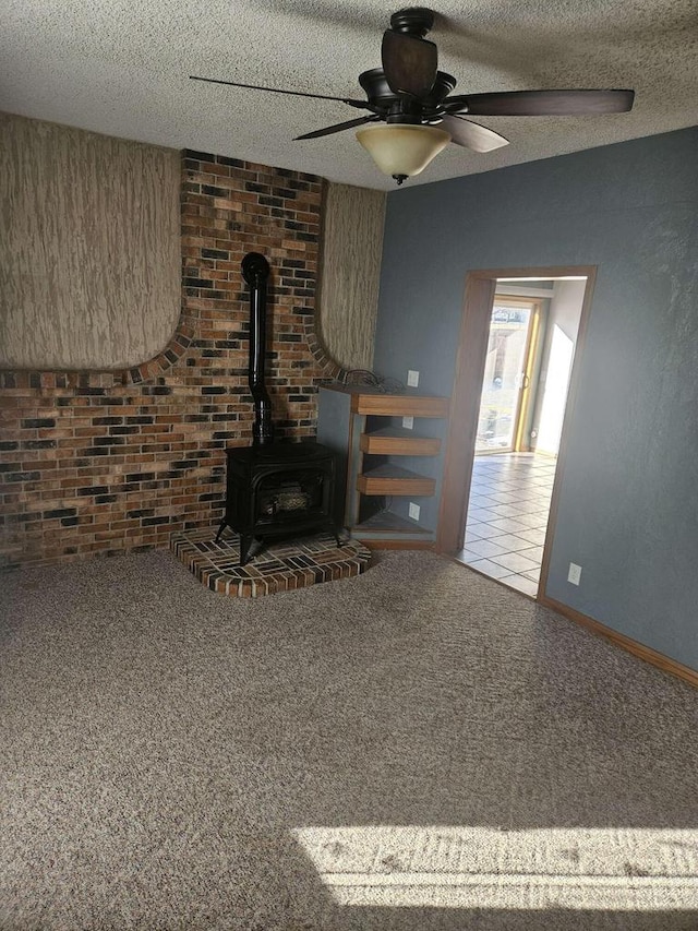 unfurnished living room with a textured ceiling, ceiling fan, carpet flooring, and a wood stove