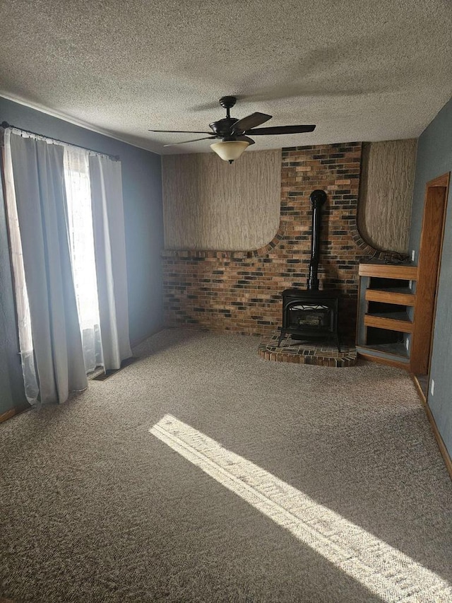 unfurnished living room featuring ceiling fan, a wood stove, a textured ceiling, and carpet flooring