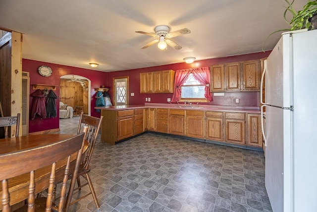 kitchen featuring arched walkways, a ceiling fan, freestanding refrigerator, a sink, and a peninsula