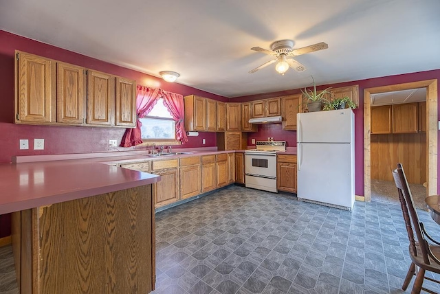 kitchen with dark floors, under cabinet range hood, a peninsula, white appliances, and a sink