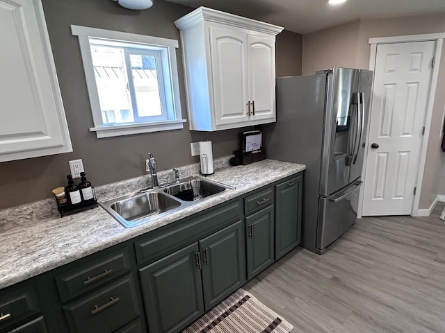 kitchen with white cabinets, stainless steel fridge, sink, and light hardwood / wood-style flooring