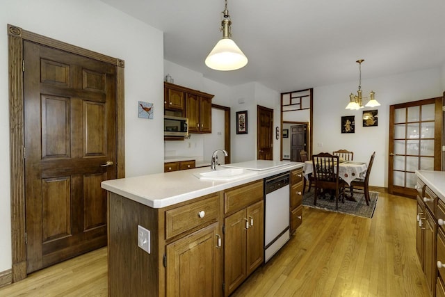 kitchen with a kitchen island with sink, sink, white dishwasher, and decorative light fixtures