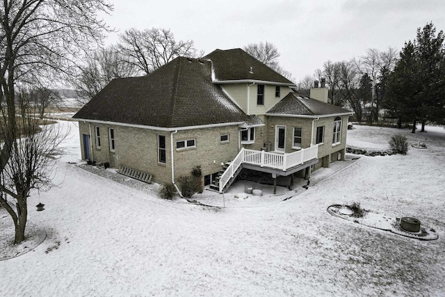 snow covered property featuring stairs, a deck, a chimney, and a shingled roof