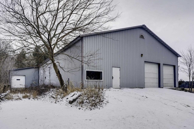 snow covered structure featuring a garage and an outdoor structure