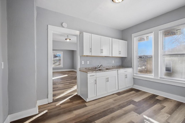 kitchen with light hardwood / wood-style floors, sink, white cabinetry, and light stone countertops