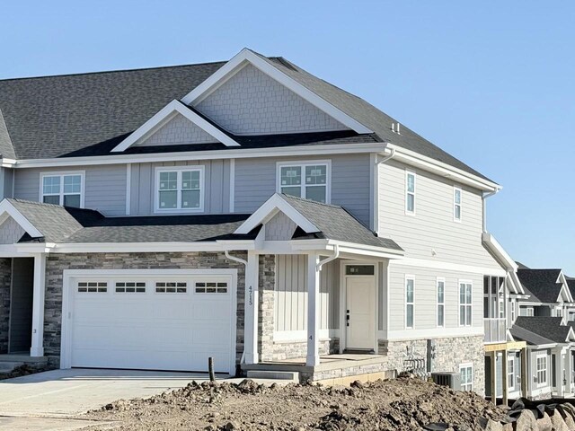 view of front of house featuring a shingled roof, concrete driveway, board and batten siding, a garage, and stone siding