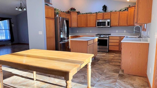 kitchen featuring an inviting chandelier, appliances with stainless steel finishes, a kitchen island, pendant lighting, and sink