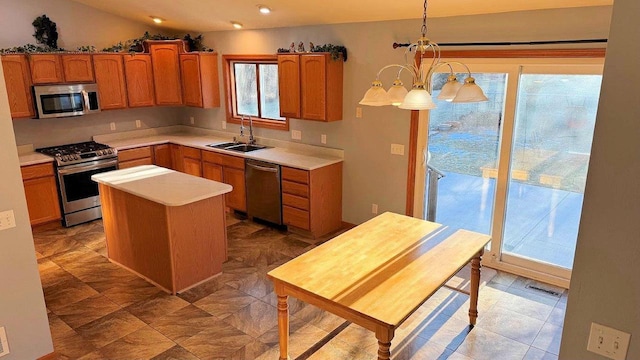 kitchen with appliances with stainless steel finishes, decorative light fixtures, vaulted ceiling, a kitchen island, and sink