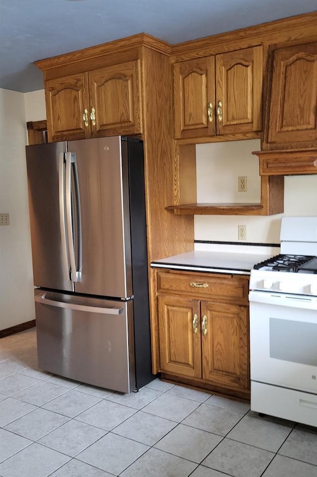 kitchen featuring white range with gas cooktop, light tile patterned floors, and stainless steel refrigerator