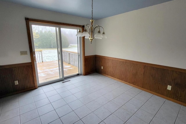 unfurnished dining area featuring light tile patterned floors, wooden walls, and a chandelier