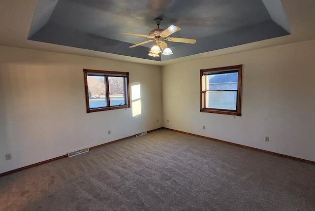 carpeted empty room with ceiling fan and a raised ceiling