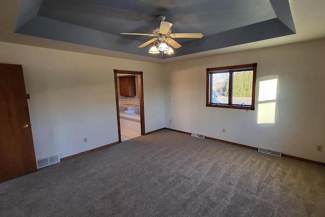 unfurnished bedroom with a tray ceiling, carpet floors, ensuite bath, and ceiling fan