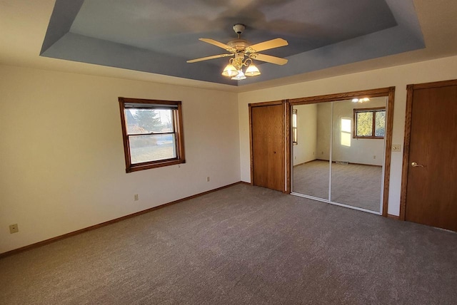 unfurnished bedroom with ceiling fan, a tray ceiling, carpet floors, and a closet