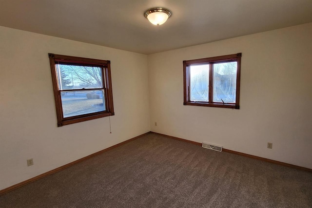 empty room featuring plenty of natural light and dark colored carpet