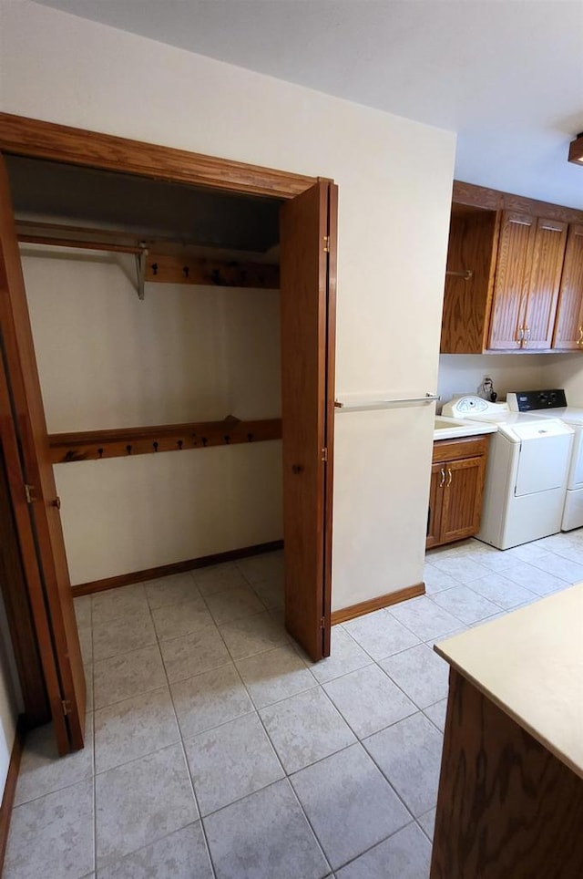 clothes washing area with washing machine and dryer, cabinets, and light tile patterned flooring