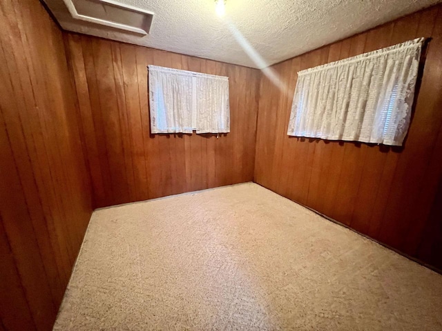 carpeted spare room with a textured ceiling and wood walls