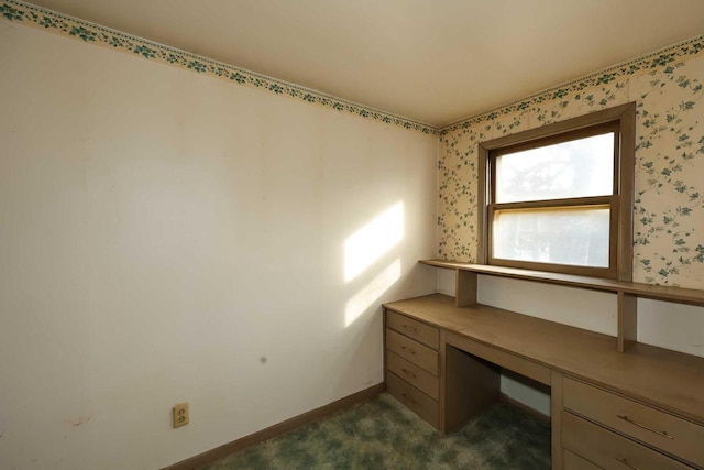 unfurnished office featuring built in desk and dark colored carpet