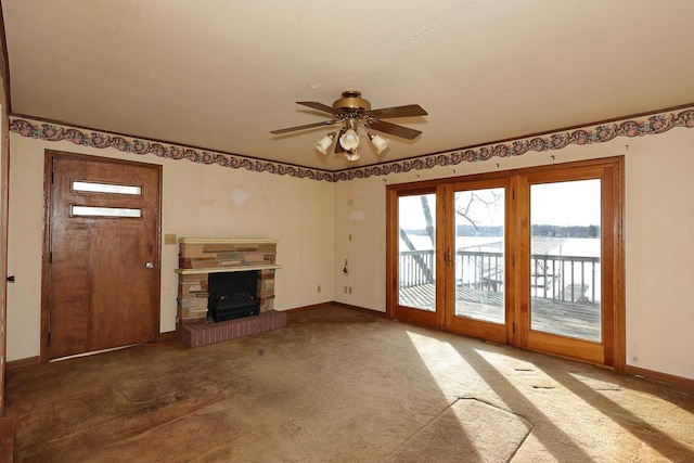 unfurnished living room with carpet flooring, a fireplace, ceiling fan, and a water view