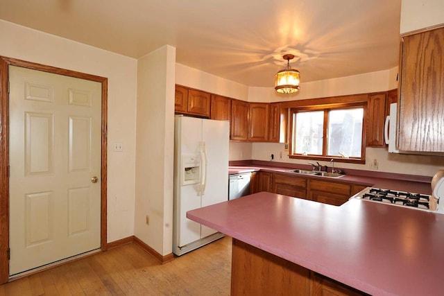 kitchen featuring pendant lighting, sink, light hardwood / wood-style floors, kitchen peninsula, and white appliances