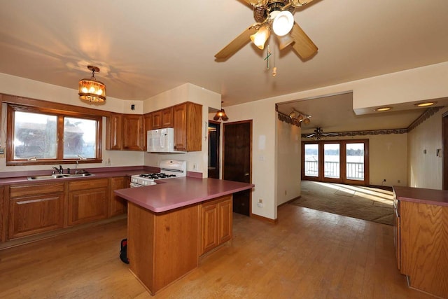 kitchen with sink, light wood-type flooring, a kitchen island, white appliances, and ceiling fan with notable chandelier