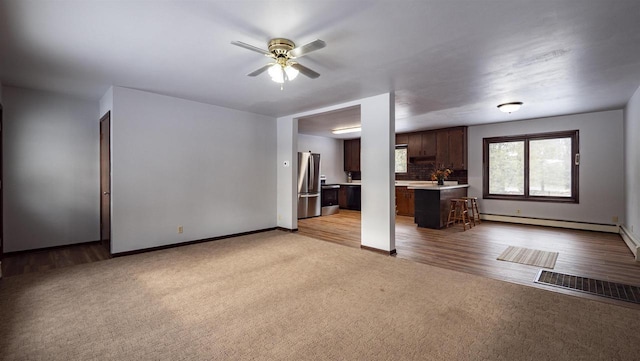 unfurnished living room featuring ceiling fan, a baseboard heating unit, and light carpet