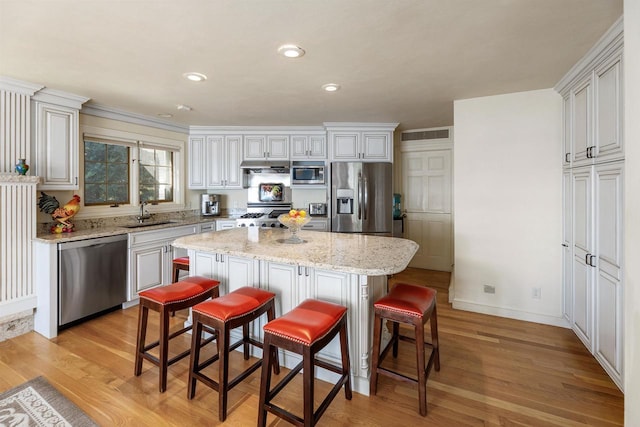 kitchen with white cabinetry, a kitchen bar, appliances with stainless steel finishes, a kitchen island, and light hardwood / wood-style flooring