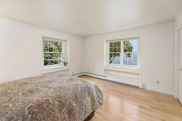 bedroom with a baseboard heating unit, a closet, and light hardwood / wood-style floors