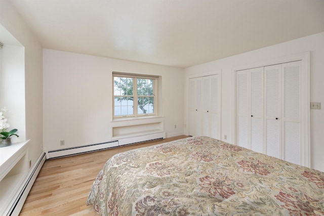 bedroom with baseboard heating, light hardwood / wood-style flooring, and multiple closets