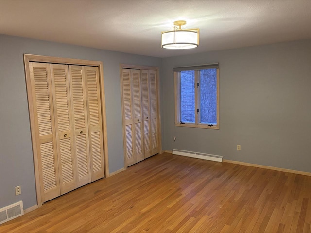 unfurnished bedroom with light hardwood / wood-style floors, baseboard heating, and two closets