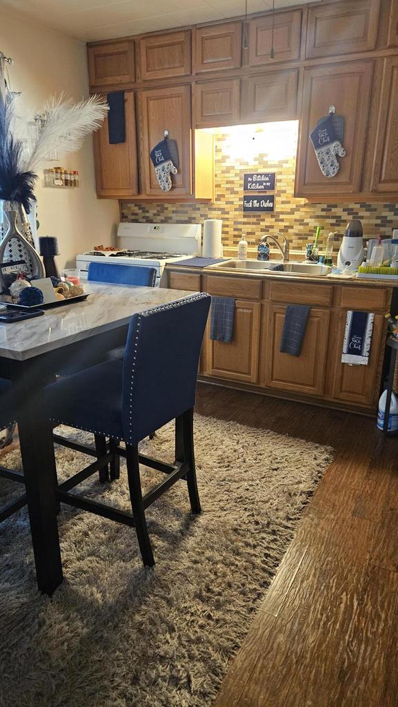 kitchen with gas range gas stove, a breakfast bar area, dark hardwood / wood-style floors, backsplash, and sink