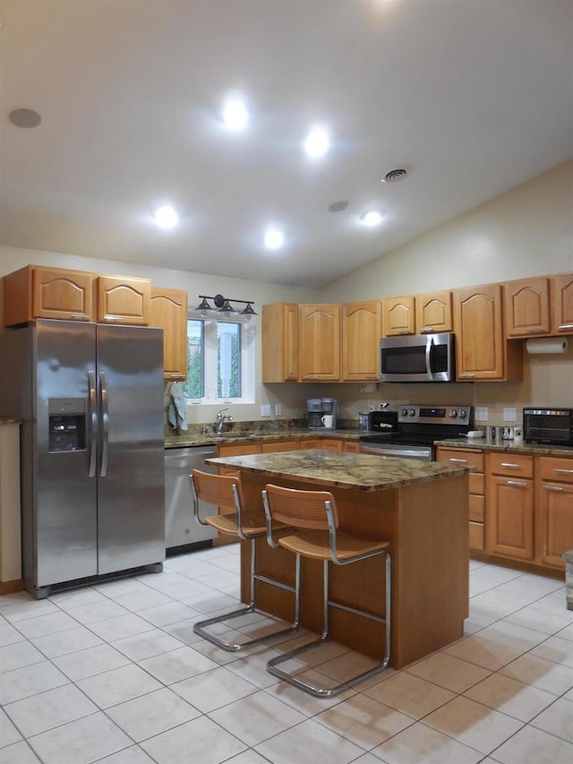 kitchen with appliances with stainless steel finishes, lofted ceiling, a kitchen island, a kitchen breakfast bar, and light tile patterned flooring