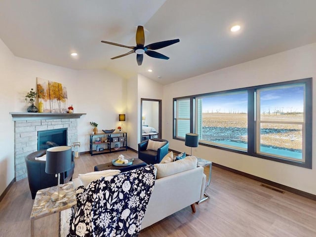 living room with ceiling fan, hardwood / wood-style floors, vaulted ceiling, and a stone fireplace